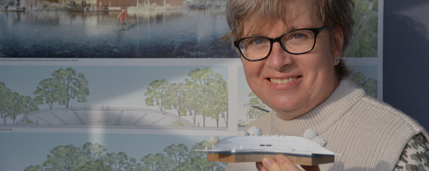 Festspiele-Mitarbeiterin Kerstin Gradert hält das Modell in Händen, das Vorbild sein soll für den Neubau der Tribüne am Großen Eutiner See. Die Pläne sind jetzt im Gastro-Pavillon der Festspiele ausgestellt. Foto: EFS